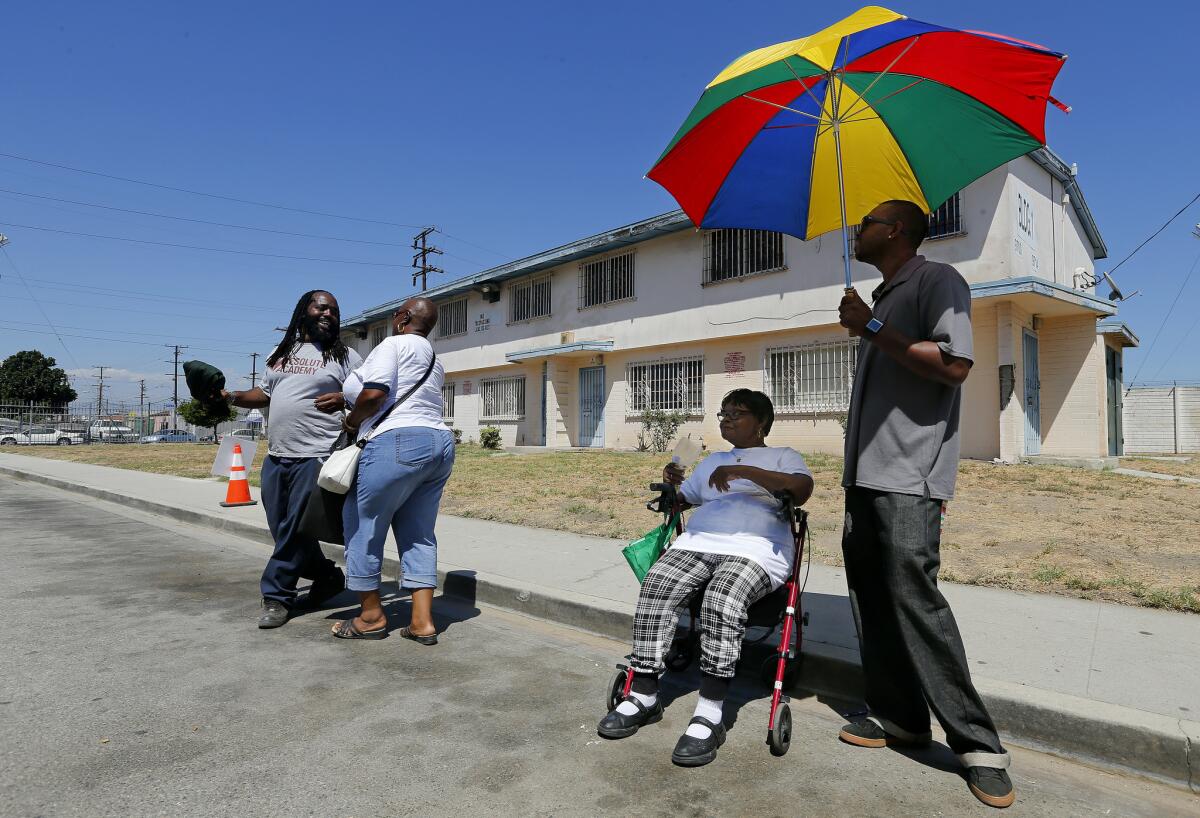 Keiandre Thompson, 25, holds an umbrella for his aunt, Mildred Martin, 76, in front of a building that will be knocked down and rebuilt as a residential home and retail space during the first phase of a project at Jordan Downs Housing Development in Watts.