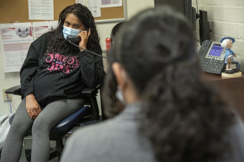 VENICE, CA-APRIL 14, 2023: Jessica Sanchez, 33, left, a medicaid patient who is 31 weeks pregnant, talks on the phone to the department of public social services about why her medicaid coverage was wrongfully terminated back on February 1, 2023. At right is Valerie Ibarra-Figueroa, a health insurance specialist at the Venice Family Clinic, who spoke on her behalf to the department of public social services to get her medicaid coverage reinstated. (Mel Melcon / Los Angeles Times)