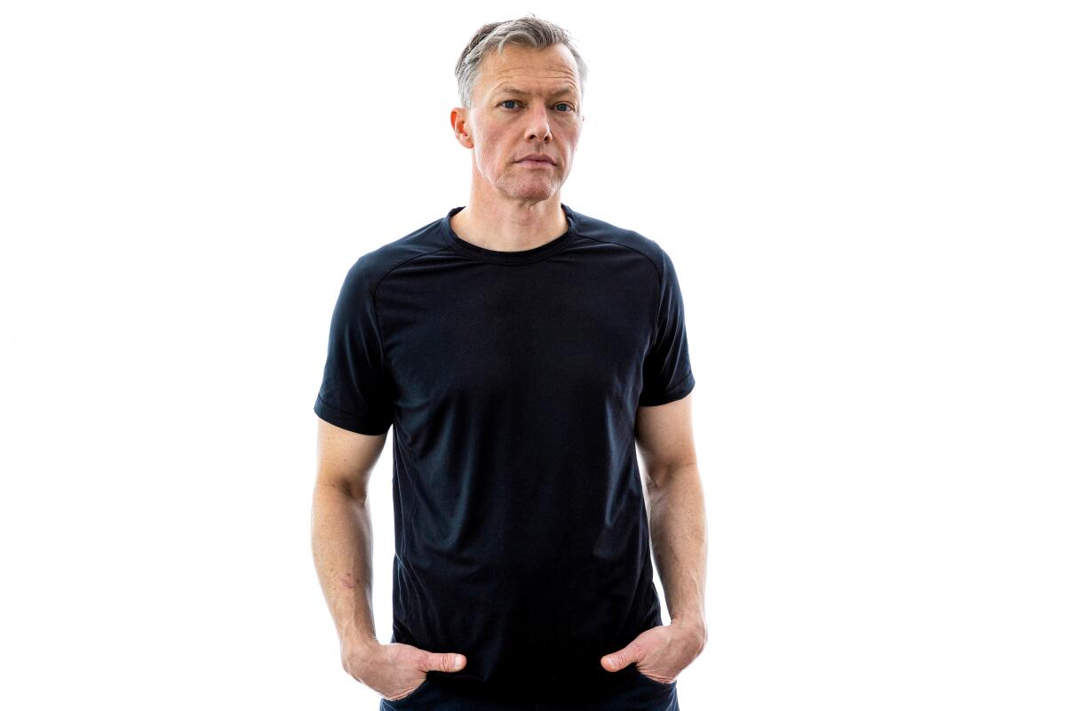 man in a black t-shirt and jeans stands with his hands in his pockets 
