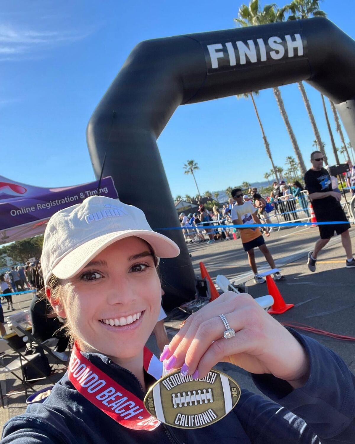 A woman holds up her 10k medal at the finish line of the 10k race.