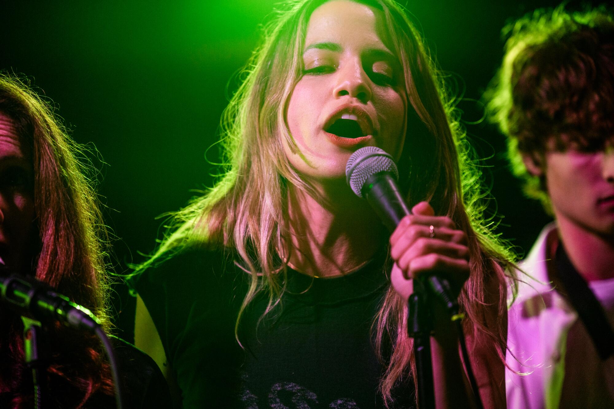 A woman cast in green lighting holds a microphone.