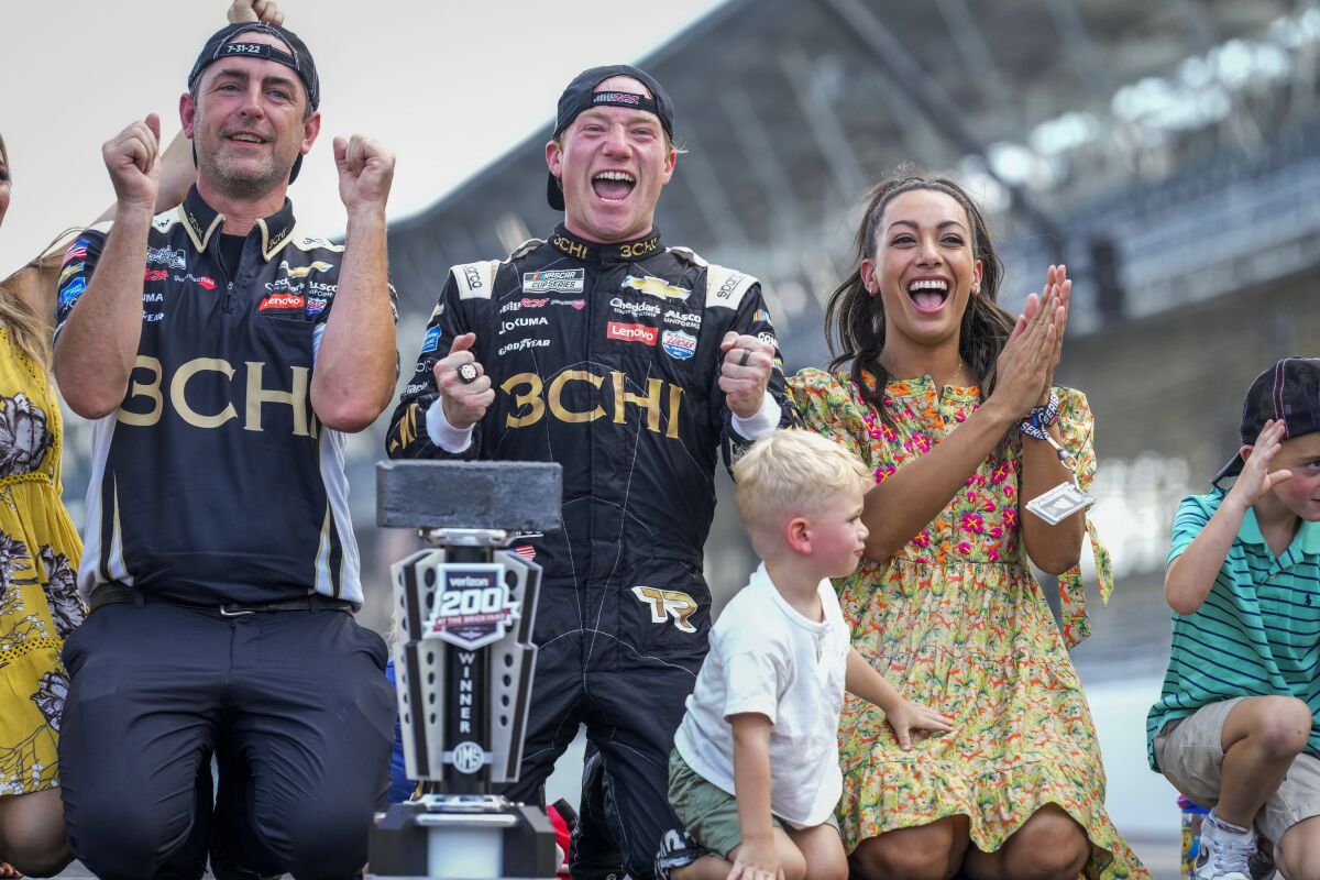 Tyler Reddick, center, and Alexa De Leon, right, celebrate after kissing the bricks following Reddick's win in the NASCAR Cup Series auto race at Indianapolis Motor Speedway, Sunday, July 31, 2022, in Indianapolis. (AP Photo/AJ Mast)