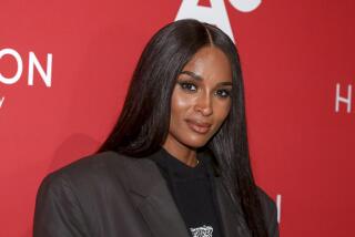 Ciara wears a dark blazer over a black shirt while posing against red backdrop