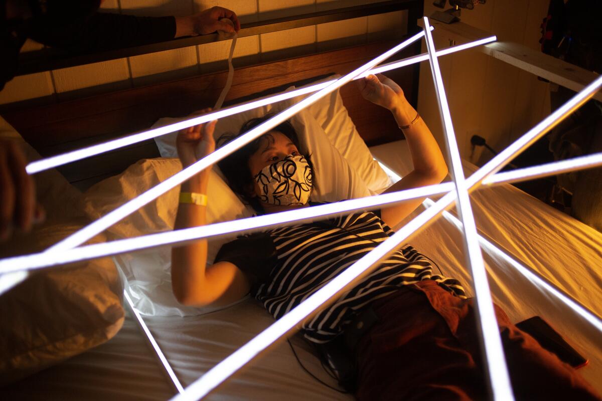 A woman in a face mask lies on her back while installing production design elements.
