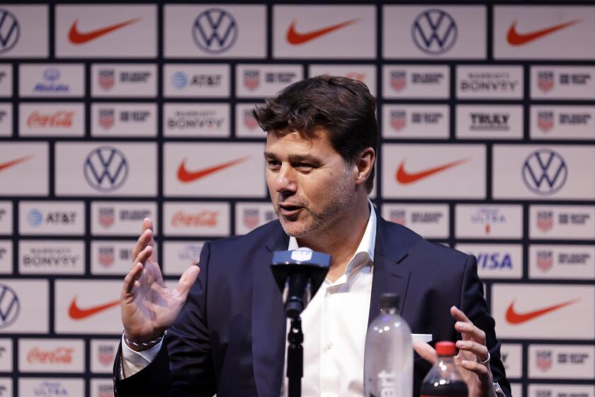 U.S. soccer coach Mauricio Pochettino sits a table and gestures with his hands while speaking at a press conference