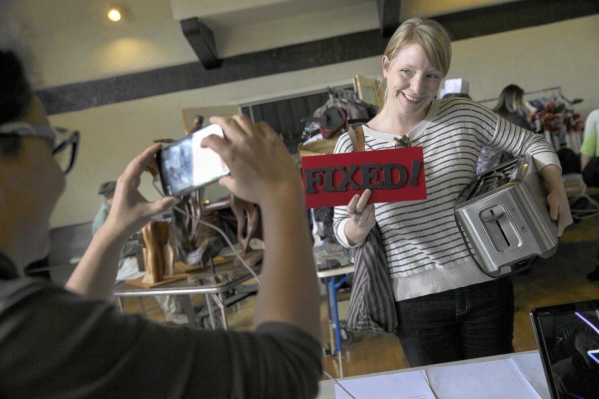 A happy Jessica Ferree poses with a "Fixed!" sign after her toaster was repaired by a volunteer at the monthly Repair Cafe event at a church hall in Pasadena.