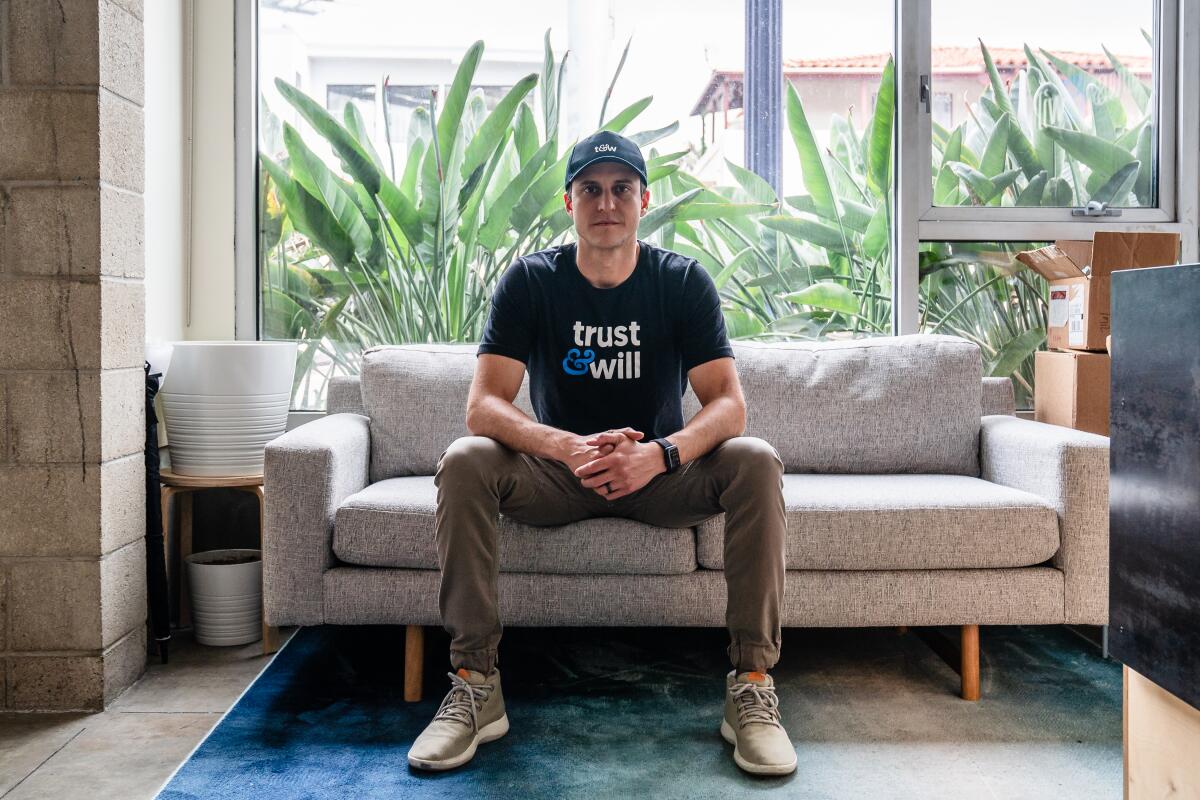 A man in a T-shirt and baseball cap sits on a couch.