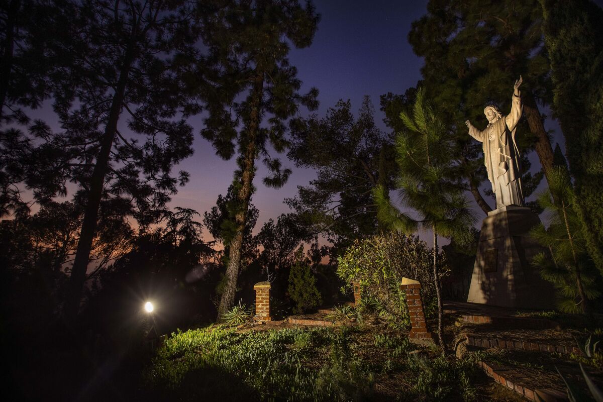 A statue of Jesus with his arms raised is lit up on the grounds of the Monastery of the Angels 