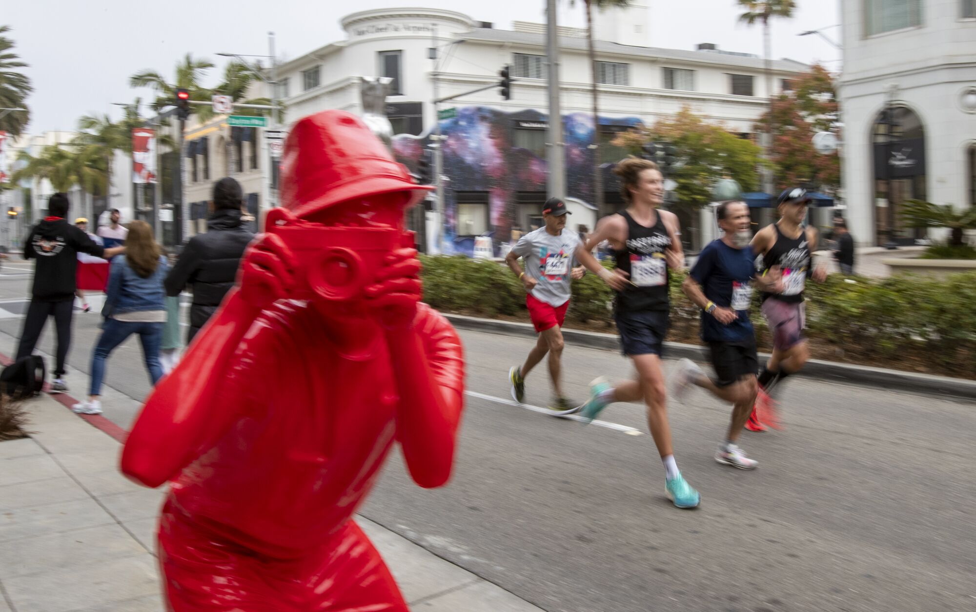 Runners pass a red statue of a camera man on Rodeo Drive