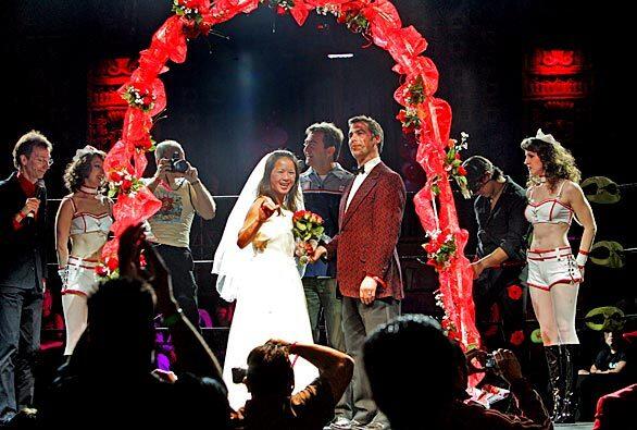 Bride Katy Ko waves to the crowd as she and her groom David Weiner are wed by Action Man Liam Gowing on a stage in front of the wrestling ring at Lucha VaVoom at the Mayan Theatre in Los Angeles Thursday, February 14, 2008. On the sidelines, the Poubelle Twins, the Kissing Bandit (right) and emcee Blaine Capatch (left) bear witness.