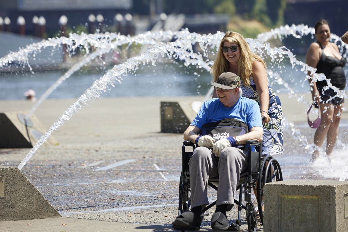 A woman pushes a man in a wheelchair near public fountains