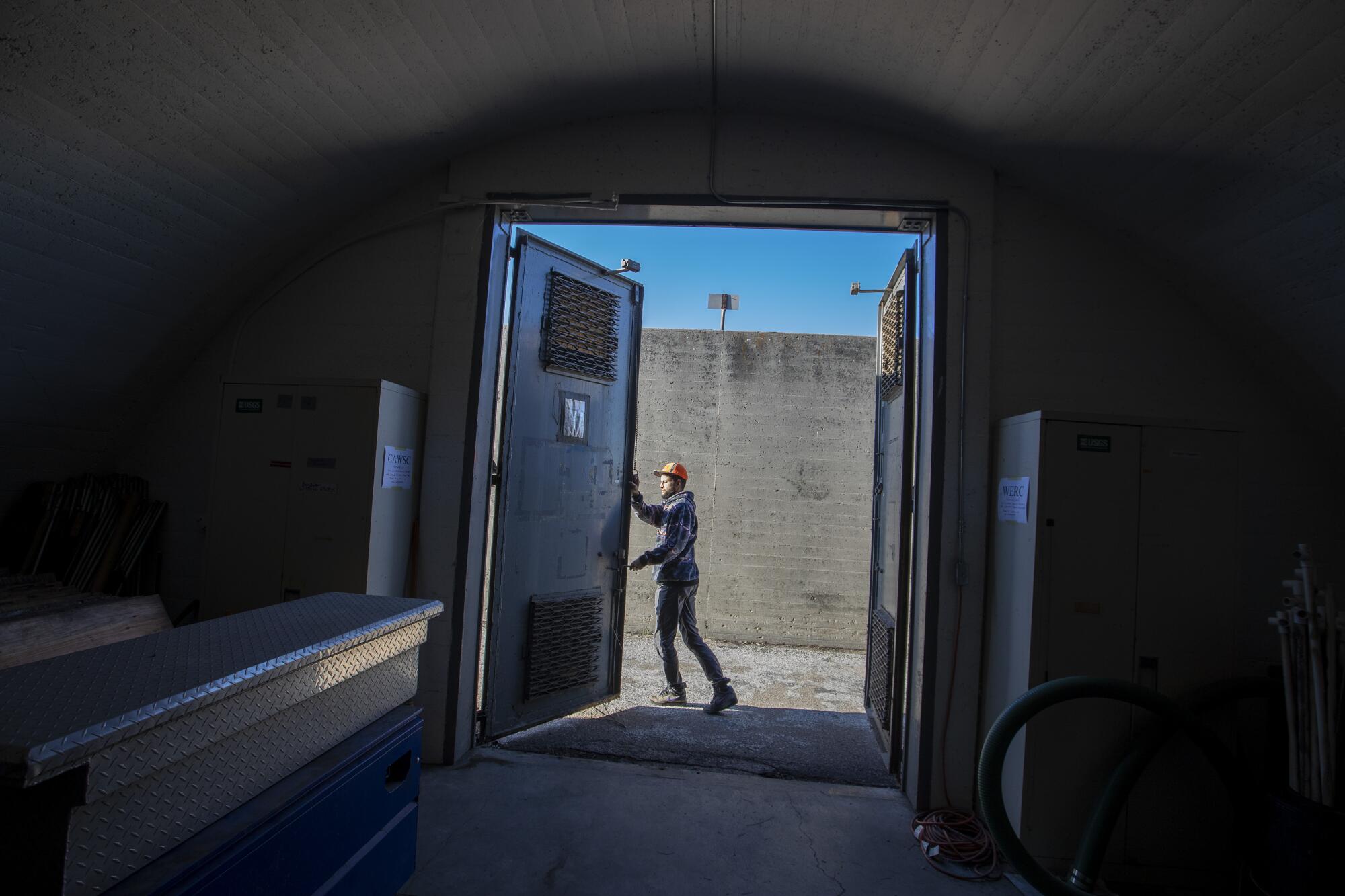 A man opens a large metal door in a dark bunker