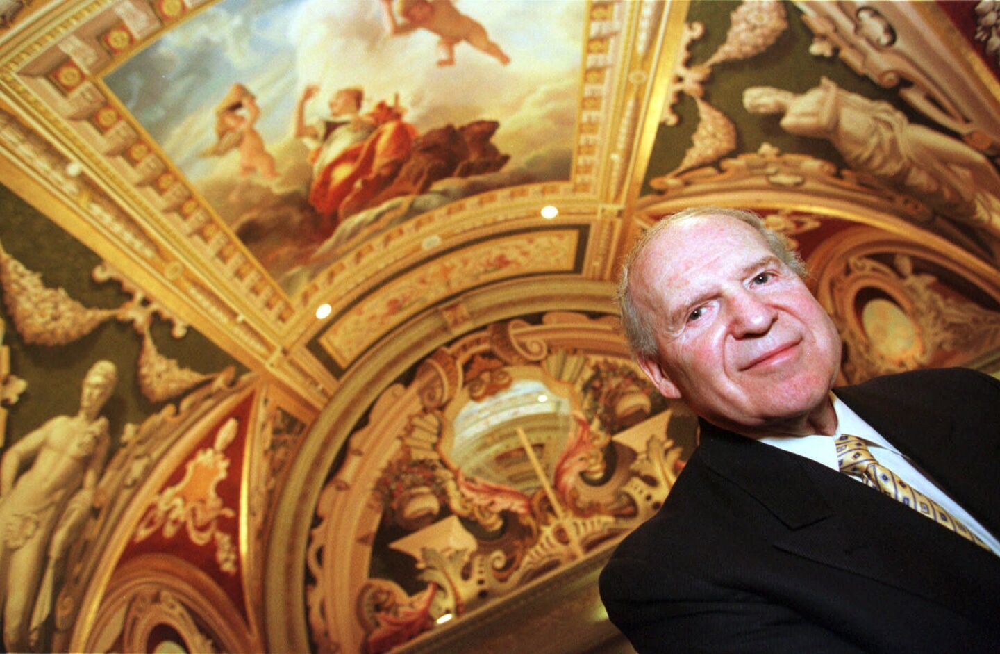 Sheldon Adelson stands beneath elaborate, gilded artwork on a ceiling.
