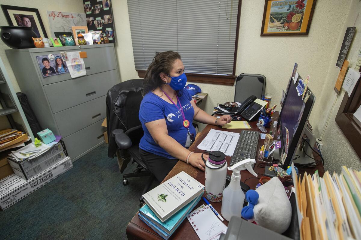 A woman works at a desk in an office wearing a mask.