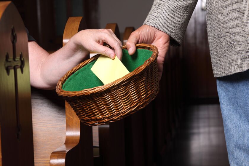 Woman's hand putting an envelope in the collection basket at church