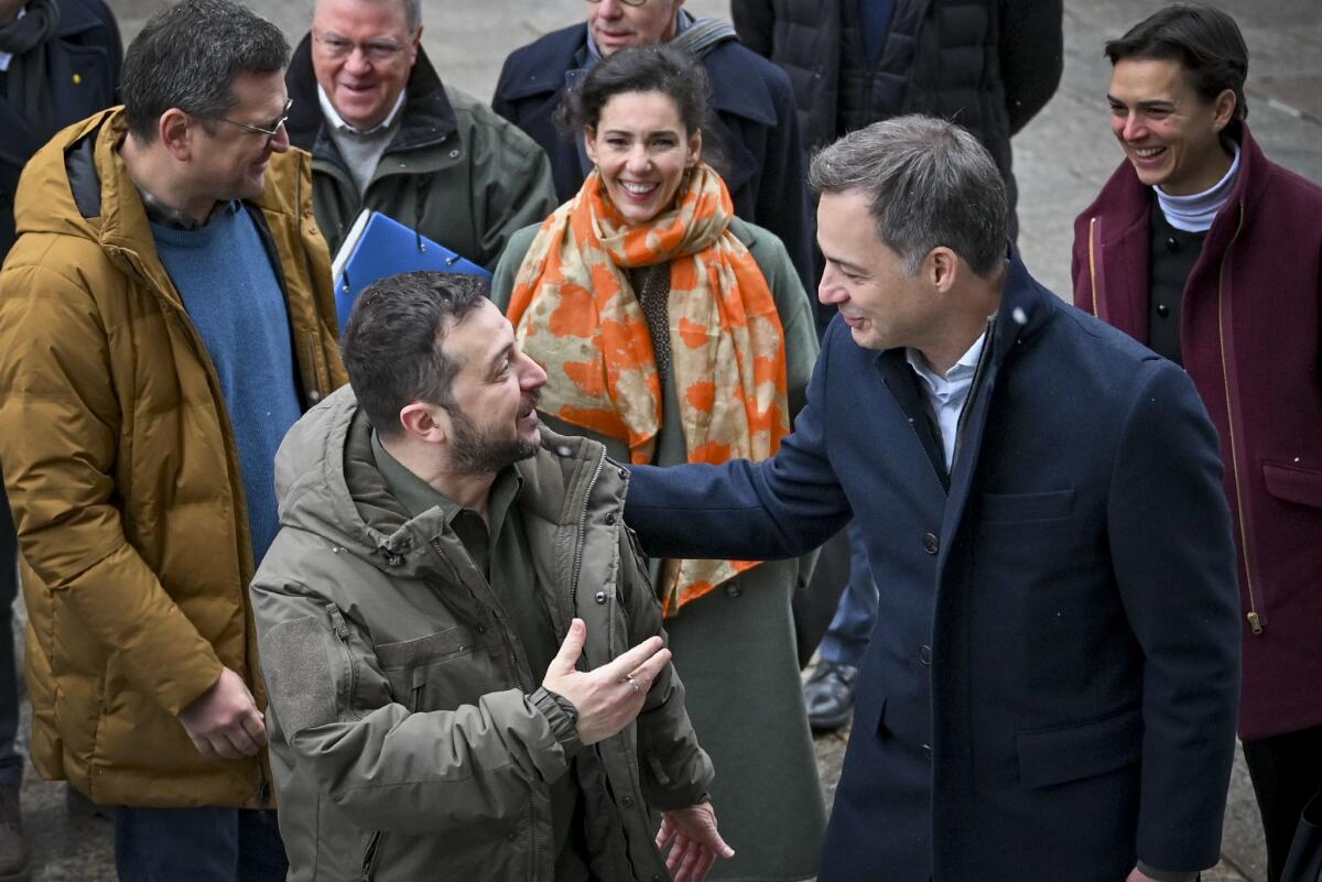 Volodymyr Zelensky, left, speaks with Alexander De Croo while other people stand behind them