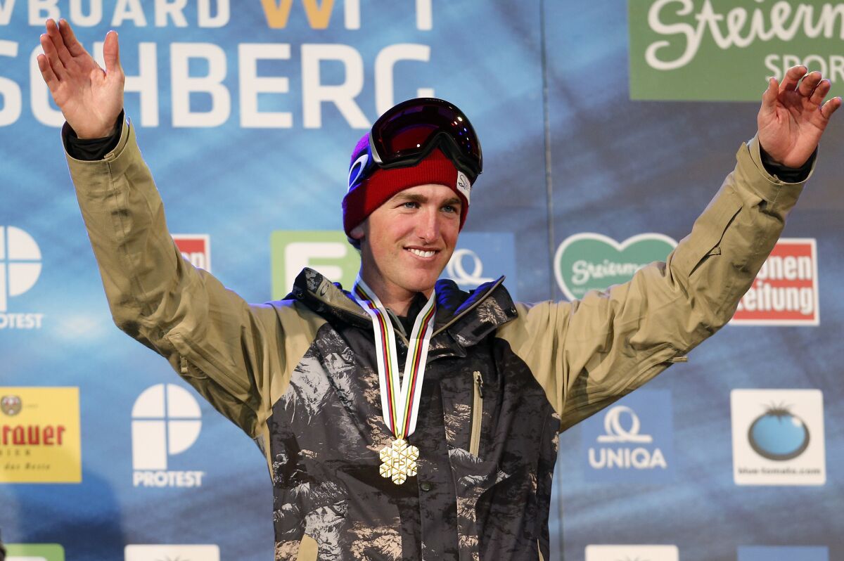 A skier raises his arms while wearing a gold medal around his neck