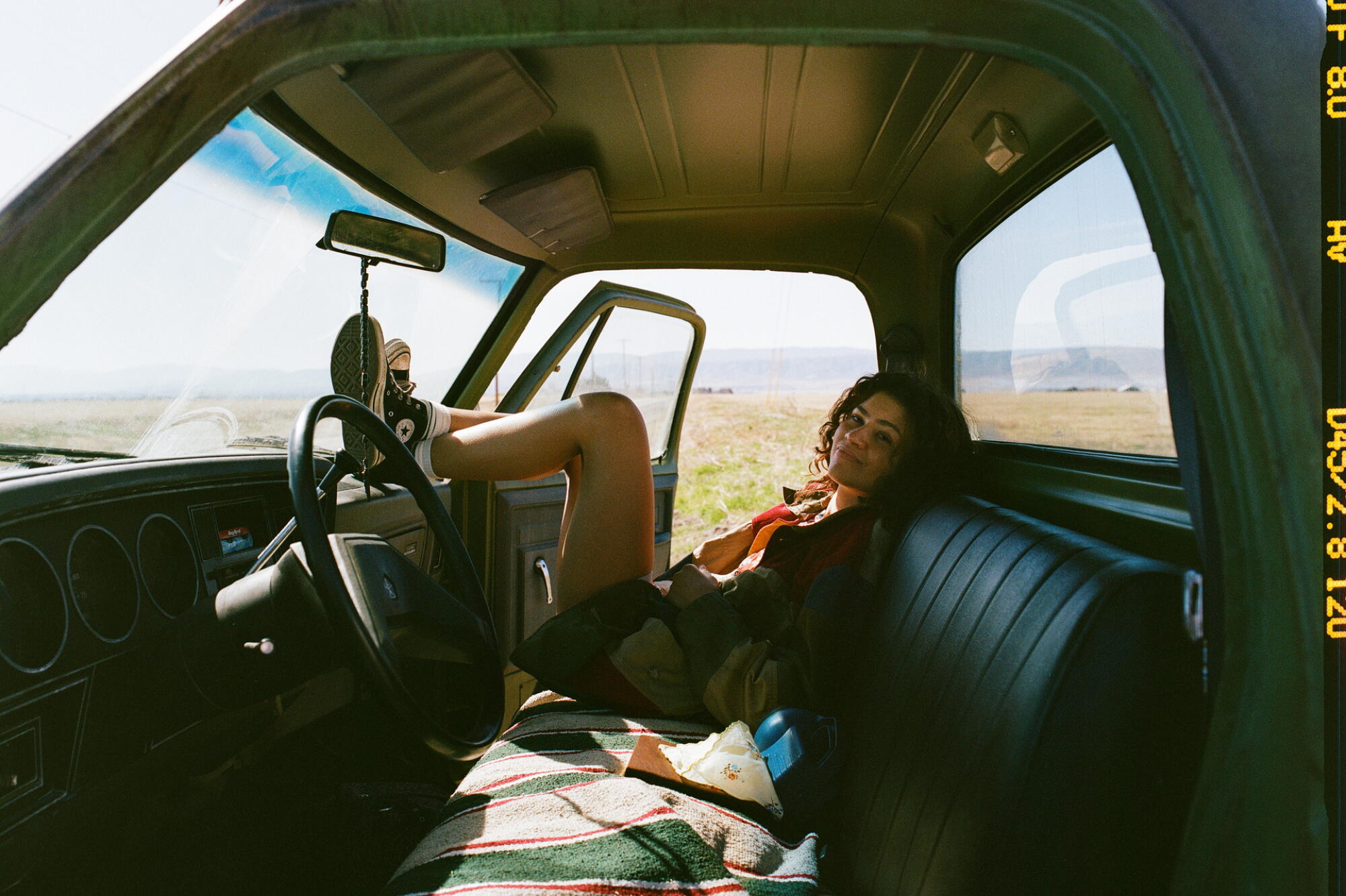 A woman sits inside the cab of a truck with her feet resting on the dash.