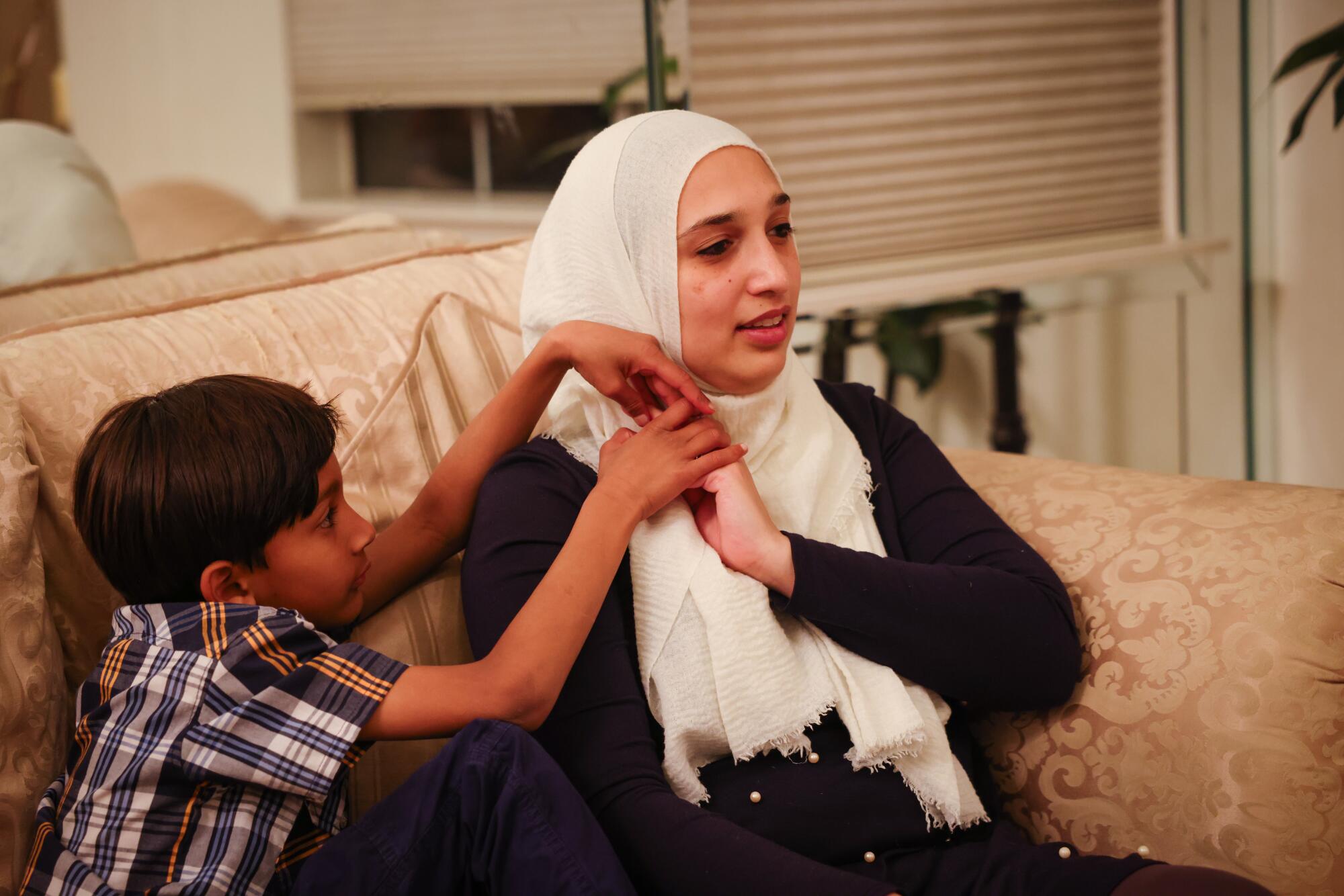 A woman in a hijab holds her son's hand while sitting on the couch. 
