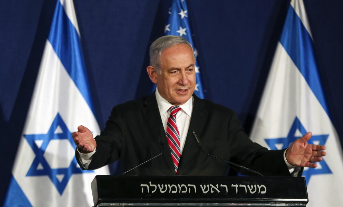 Israeli Prime Minister Benjamin Netanyahu stands at a lectern with his arms outstretched and two Israeli flags behind him.