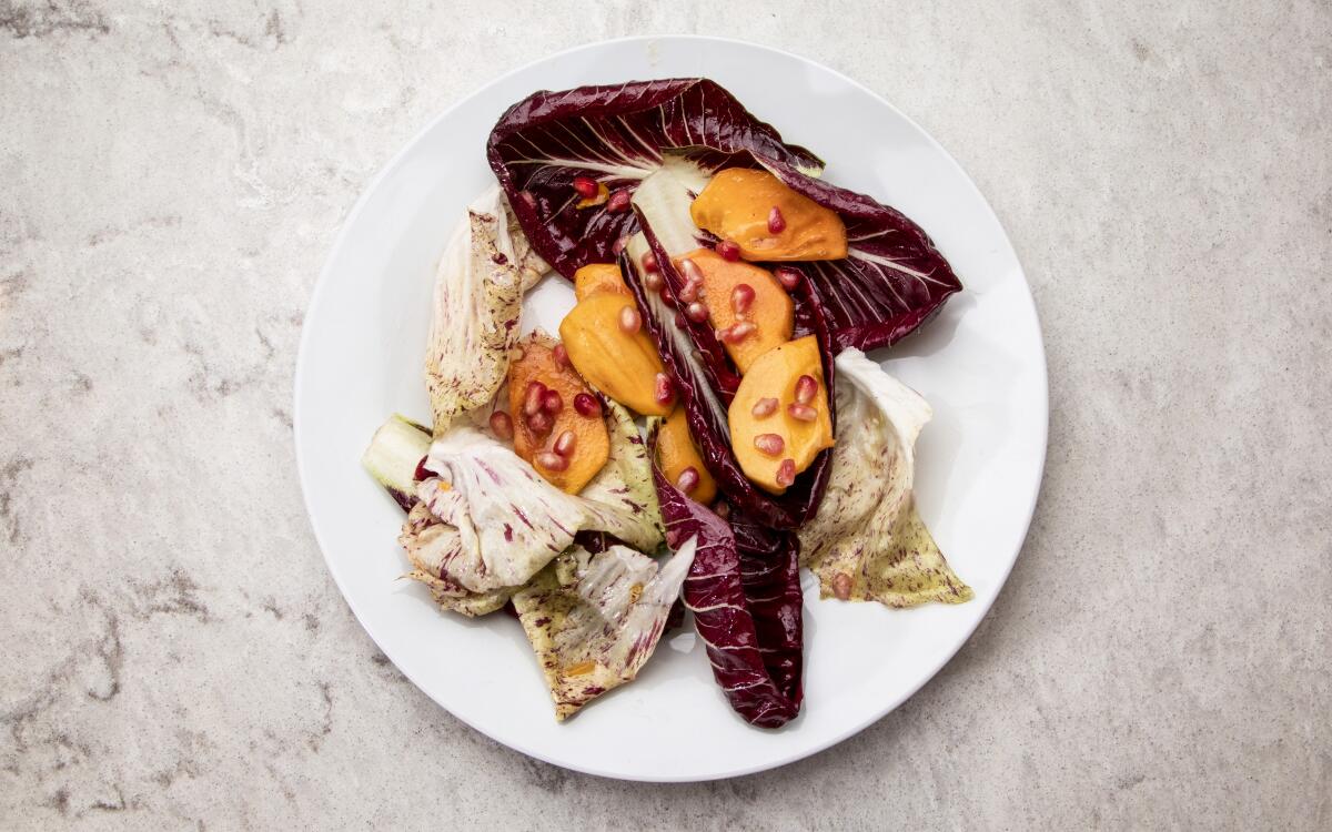 A dish of persimmons, pomegranate seeds and bitter lettuces