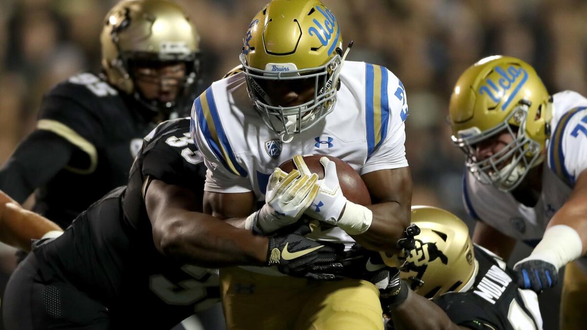 UCLA's Joshua Kelley carries the ball in the first quarter against Colorado's Javier Edwards (33) and Chris Mulumba (16) at Folsom Field on Friday in Boulder, Colo.