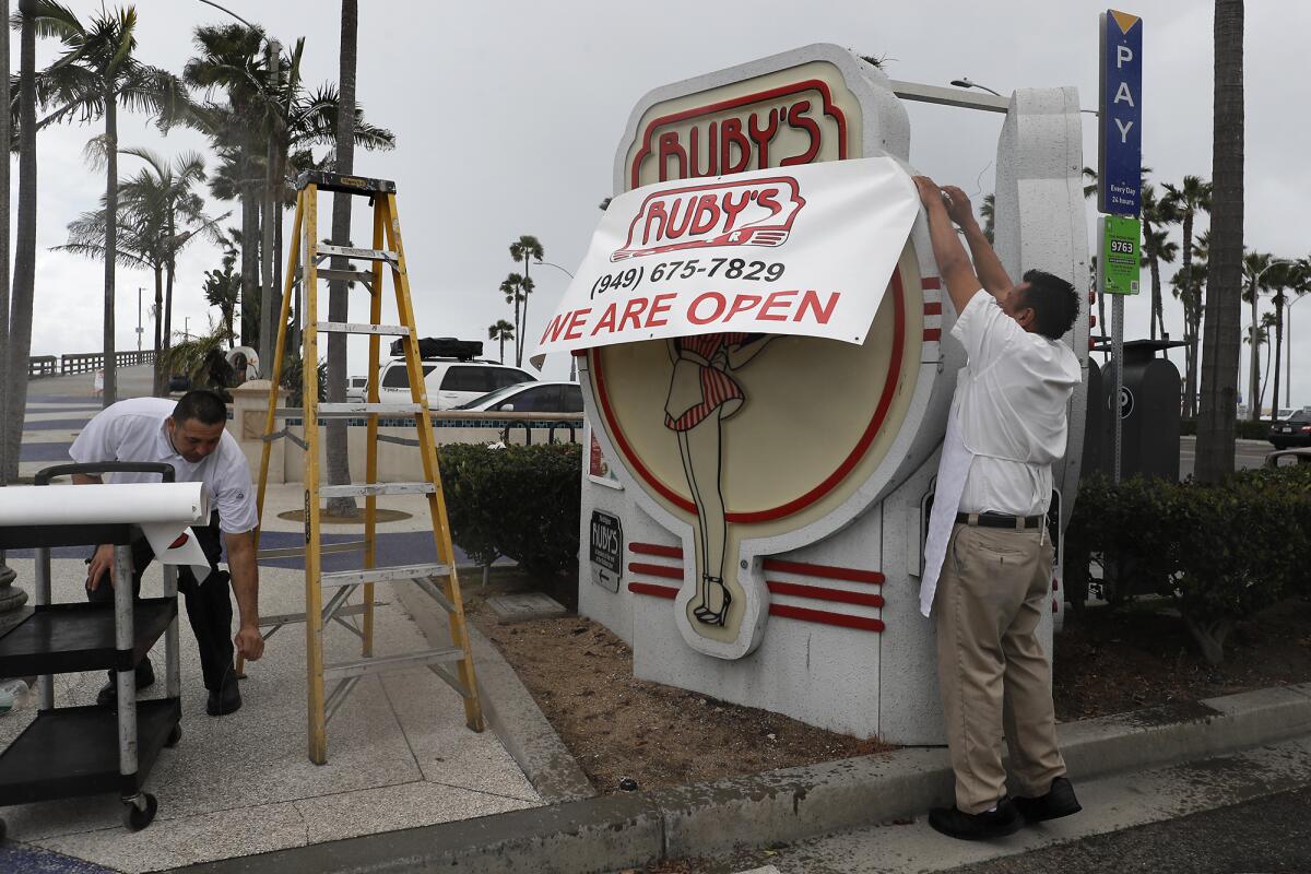 Ruby's Diner workers put up a banner notifying patrons that the restaurant is open for business at the Balboa Pier in Newport Beach, though it is only taking to-go orders.