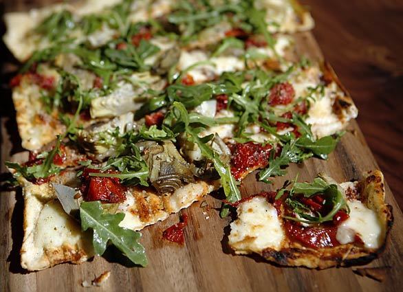 This market flatbread is topped with artichokes, smoked mozzarella and roasted tomatoes with a flurry of zigzag-y arugula leaves on top.