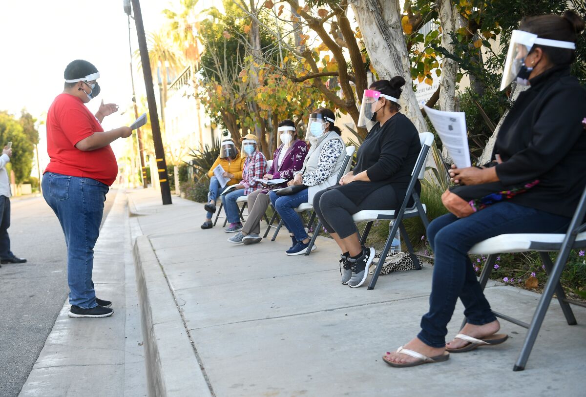 Housekeeping workers sit in plastic chairs in a row with face shields and masks as a union staff member speaks to them