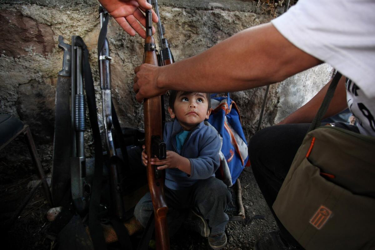 In this Thursday, Jan. 16, 2014 photo, a child tries to help his father arrange weapons at a checkpoint set up by the Self-Defense Council of Michoacan in Tancitaro, Mexico.