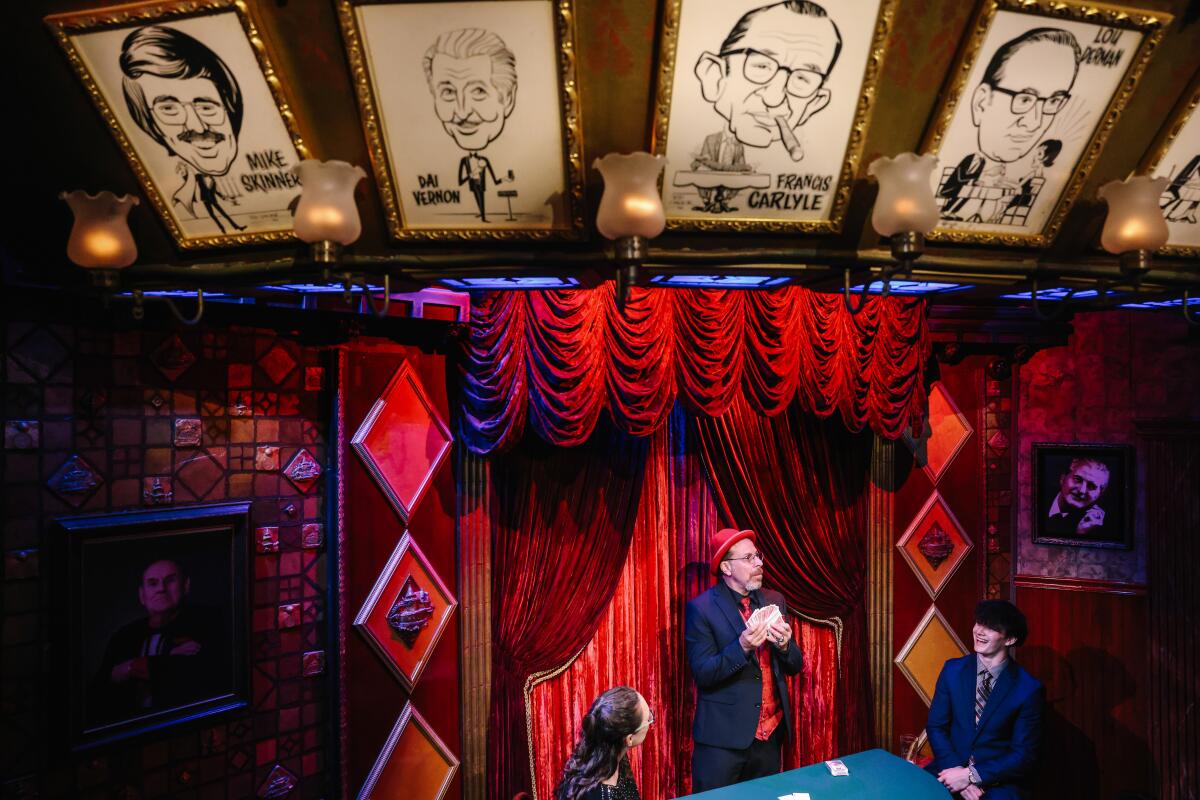 A magician performs on a stage with red curtains and caricatures overhead