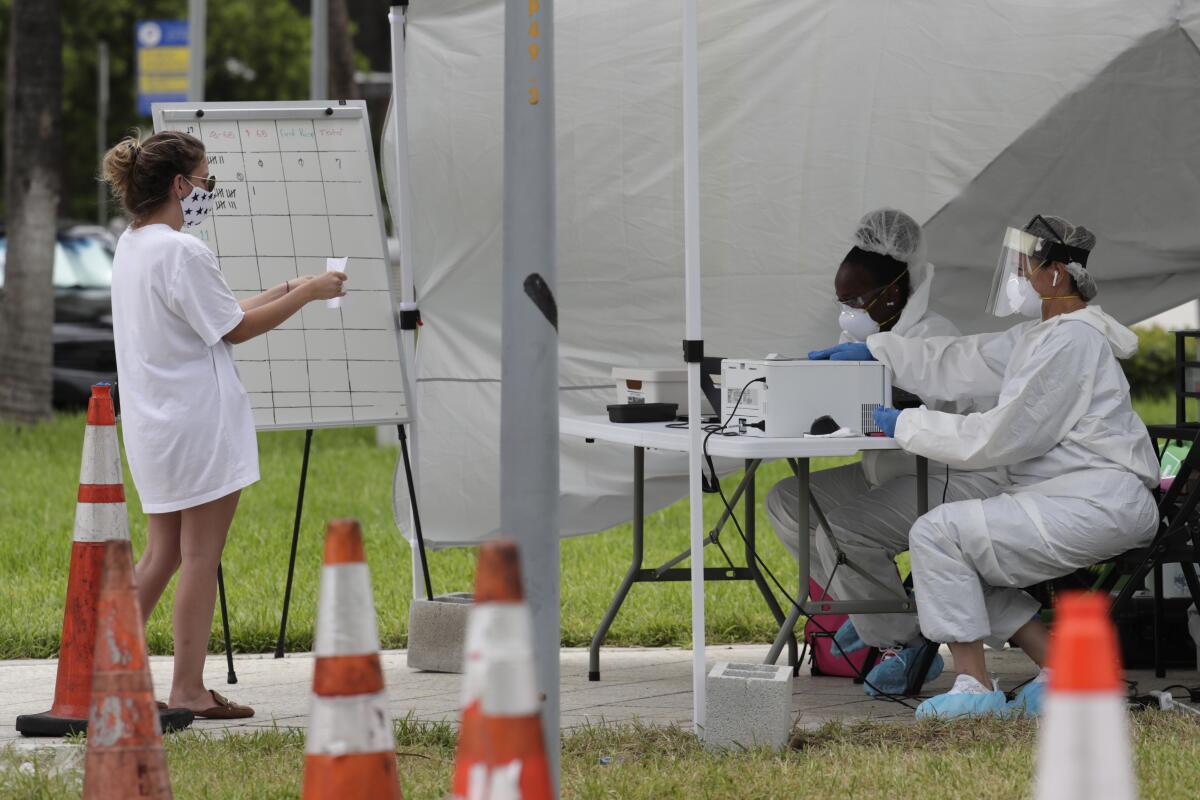 Wforkers in protective gear talk with a woman at a walk-up COVID testing site in Miami Beach, Fla. 