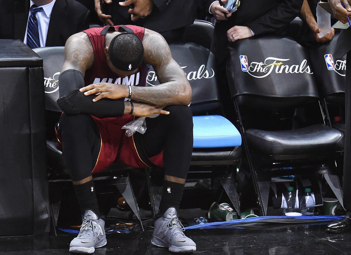 LeBron James sits on the bench because of cramps during Game 1 of the NBA Finals against the San Antonio Spurs on Thursday.