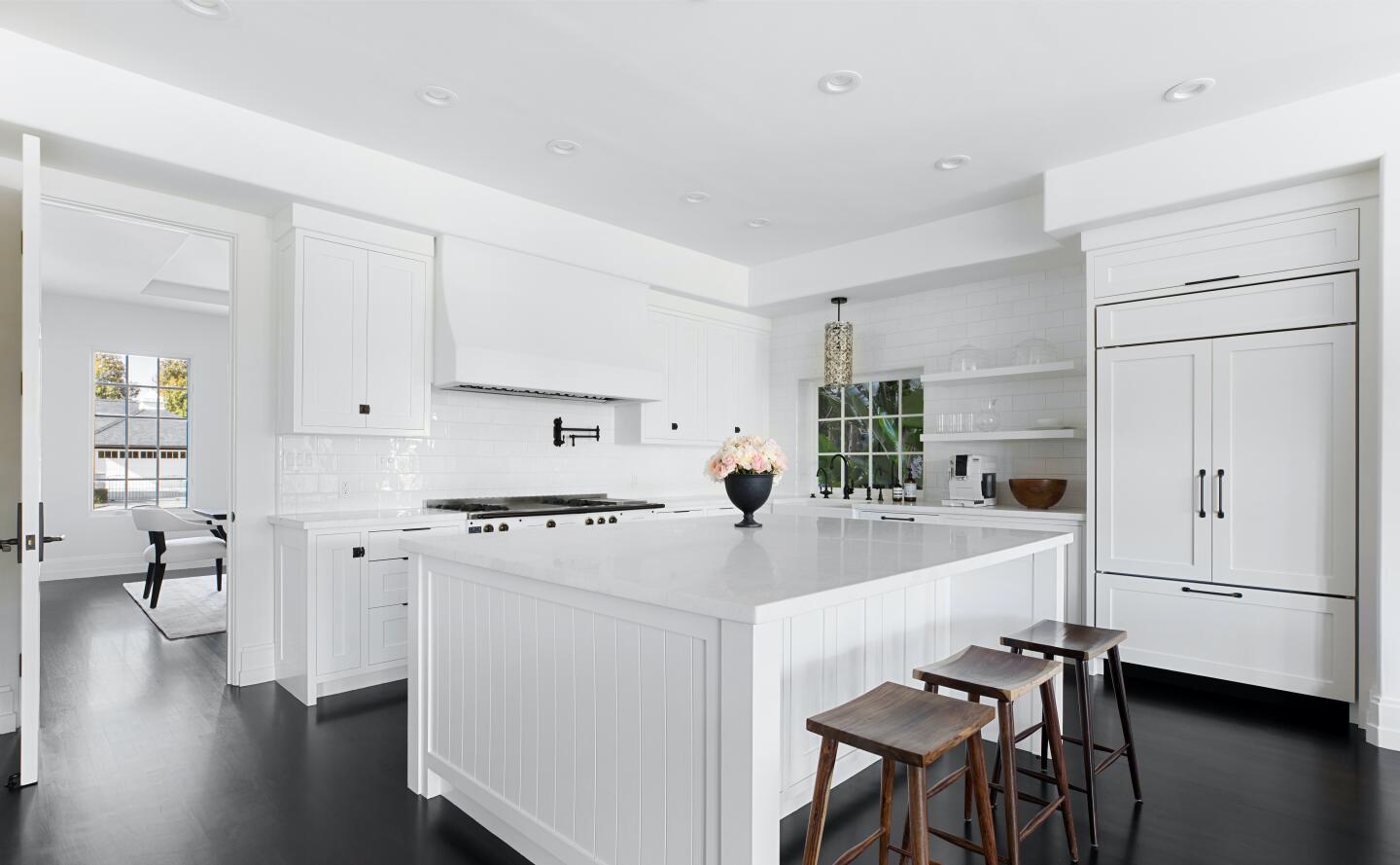 White walled kitchen with an island and chairs, appliances and dark wood flooring.