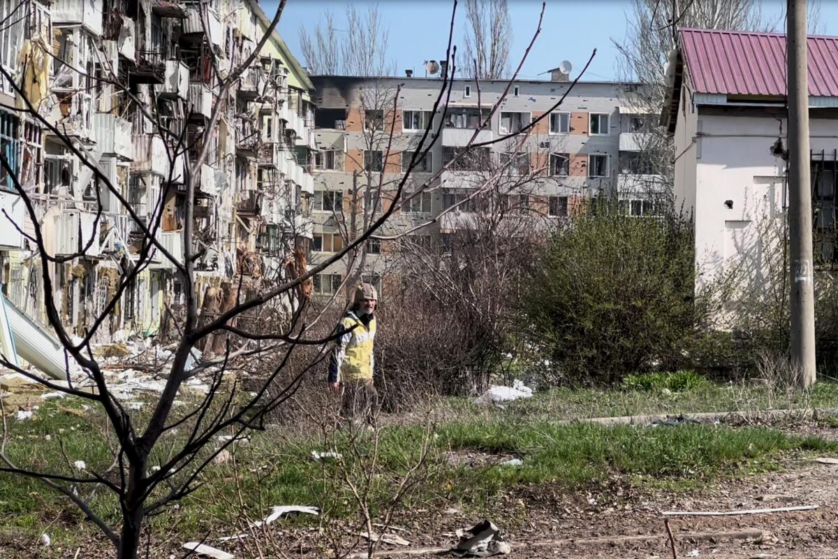A lone man walks near damaged residential apartment buildings. 