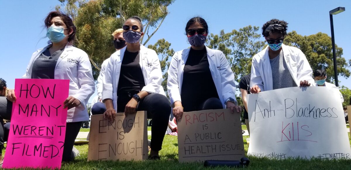 Four medical students kneel and hold anti-racism signs.