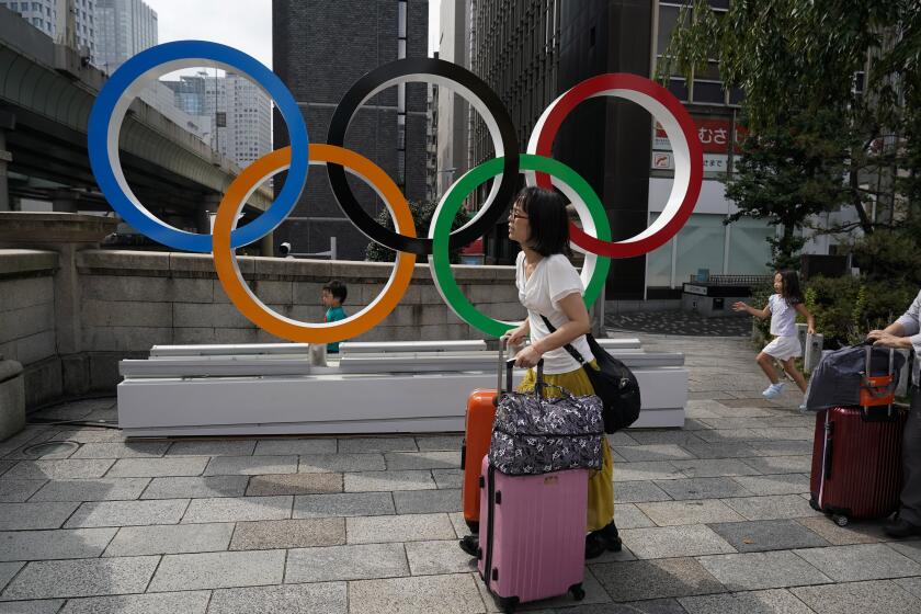 En esta foto del lunes 19 de agosto de 2019, turistas cargan sus valijas frente a anillos olímpicos en Tokio. (AP Foto/Jae C. Hong) ** Usable by HOY, ELSENT and SD Only **