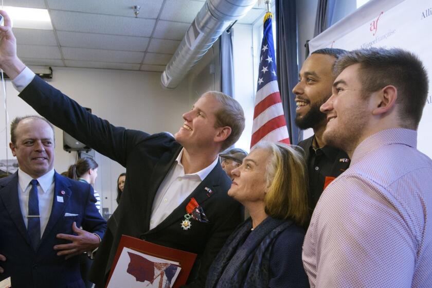 Spencer Stone, left holding the camera, photographs himself and French Conseillere Consulaire Sophie Lartilleux-Suberville, Anthony Sadler, and Alek Skarlatos following a French Naturalization Ceremony in Sacramento, Calif., Thursday, Jan. 31, 2019. The three men were heralded as heroes when they subdued an armed terrorist on a train in France in 2015. Today they were granted French citizenship. (AP Photo/Randall Benton)