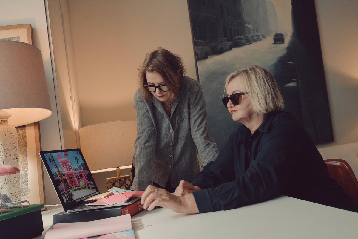 Two women look at a laptop screen with multiple pink color chips on the table.