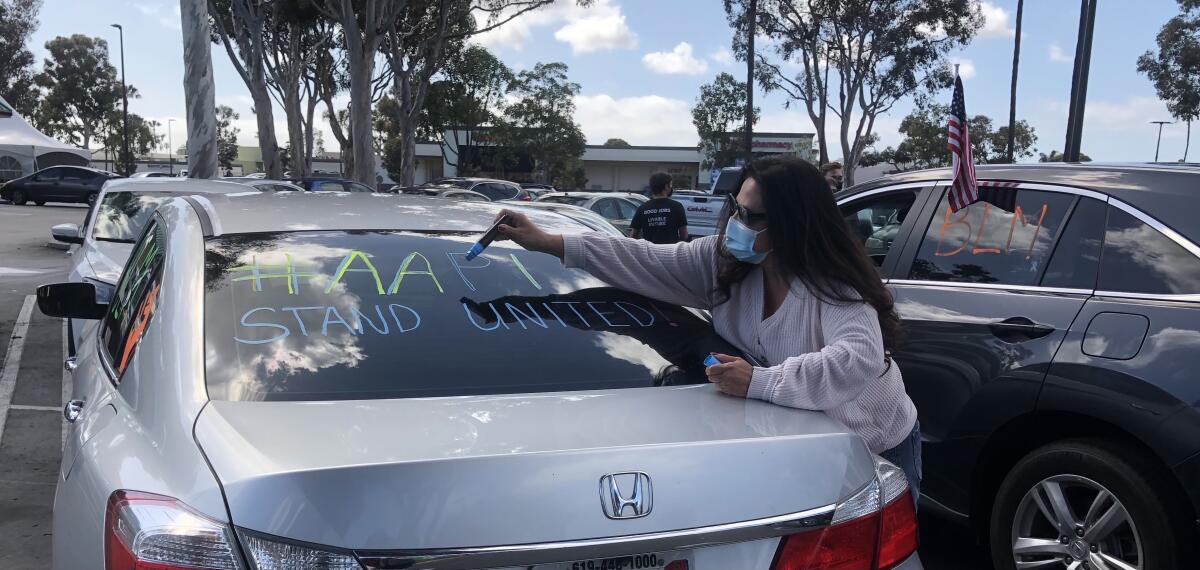 Roseanna Rosette writes a message on a car before a caravan of cars rallied against anti-Asian hate