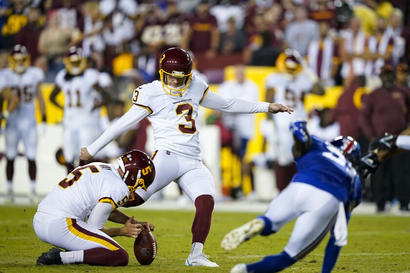 Washington Football Team kicker Dustin Hopkins kicks as punter Tress Way holds the ball.