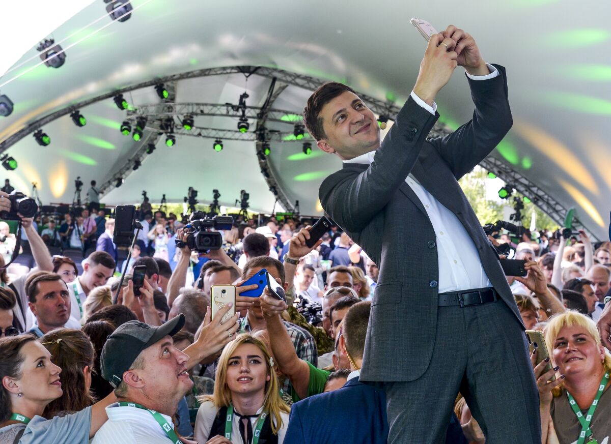 FILE Ukrainian President Volodymyr Zelenskyy takes a selfie at the first congress of his party called Servant of the People in the city Botanical Garden, Kiev, Ukraine, Sunday, June 9, 2019. As a political novice running to be Ukraine’s president, Volodymyr Zelenskyy vowed to reach out to Russia-backed rebels in the east who were fighting Ukrainian forces and make strides toward resolving the conflict. The assurances contributed to his landslide victory in 2019. (AP Photo/Zoya Shu, File)