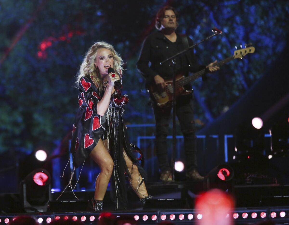 Carrie Underwood performs onstage in a black jacket covered with red hearts.