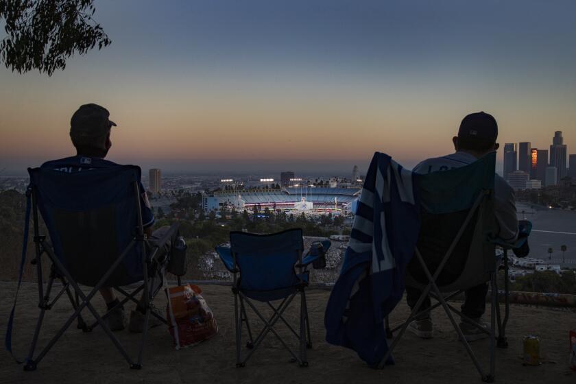LOS ANGELES, CA - AUGUST 8, 2020: Season ticket holder Keith Hupp, left, and David Lopez, right, watch the Dodgers play the San Francisco Giants from a far overlook spot because of the coronavirus pandemic in Elysian Park on August 8, 2020 in Los Angeles, CA. They are listening to the game on the radio since they are too far away to hear the sounds form the game. No fans are allowed in the stadium.(Gina Ferazzi / Los Angeles Times)