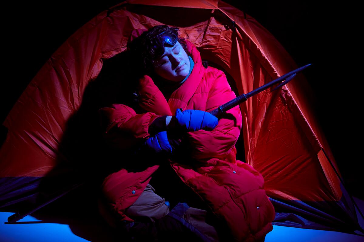 Someone sitting outside a tent, holding a spear.