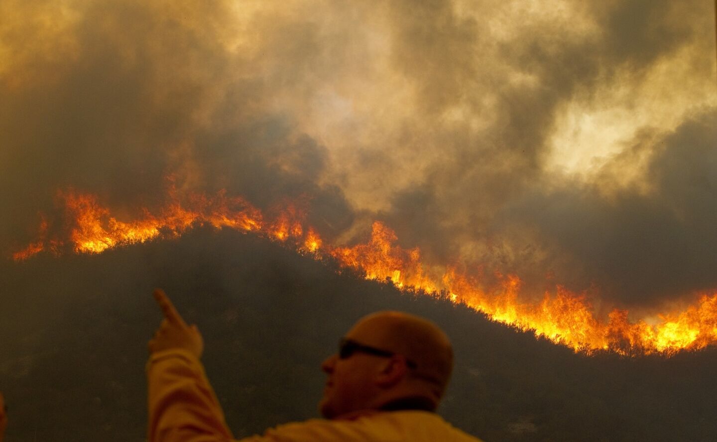 A freelance photographer points to active flame as a hillside burns.