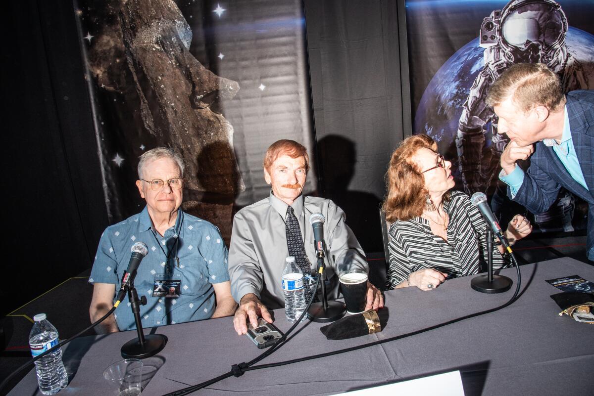 Four people sitting at a table in front of microphones.
