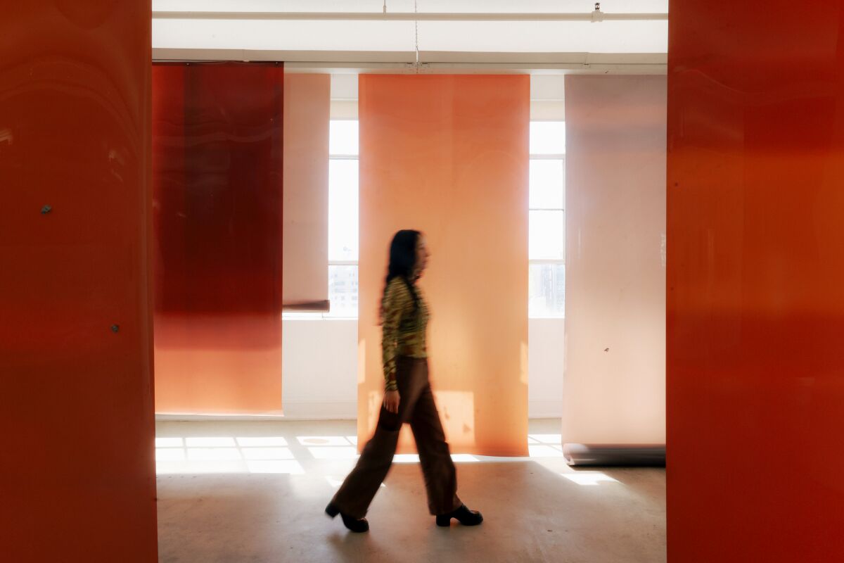 Laurie Kang is seen walking through sheets of her flesh-colored works in a warehouse art studio.