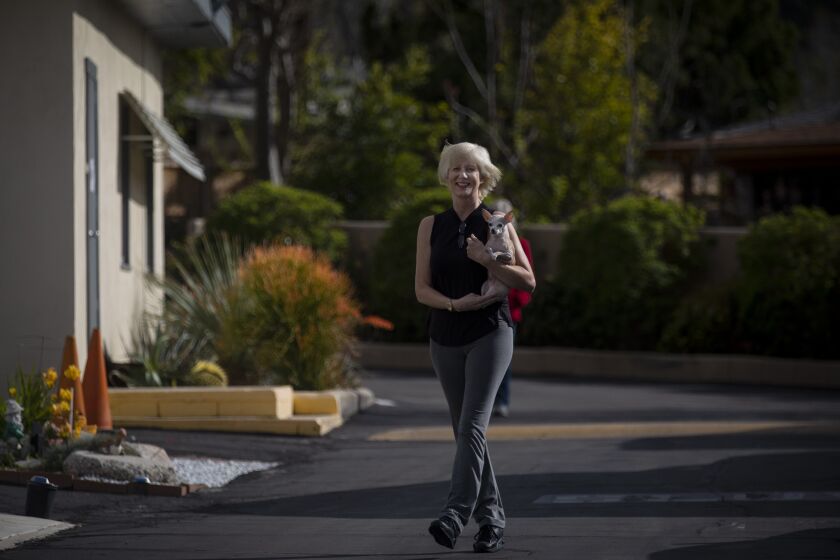 SUNLAND, CALIF. - MARCH 19: Tina Smith, of Sunland, iwalks out of her home with her dog "Chica" in Sunland, Calif Thursday, March 19, 2020. She has been laid off from her waitressing job due to coronavirus epidemic. Los Angeles Times Steve Lopez, left, is social distancing outdoors while interviewing Tina Smith. (Francine Orr / Los Angeles Times)