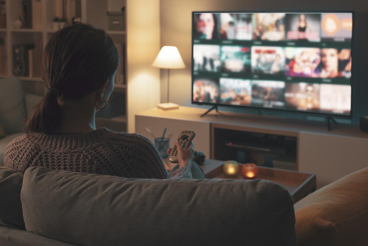 A woman holding a remote control and watching TV